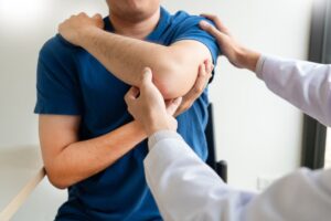 Healthcare professional addressing shoulder pain: Physiotherapist providing care and examination to a patient in a clinic or medical office setting.